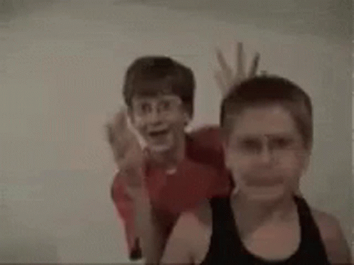 A Couple Of Young Boys Are Standing Next To Each Other . GIF