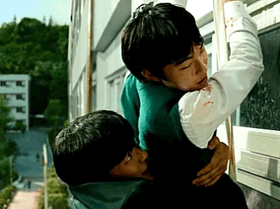 A Couple Of Young Men Are Hugging Each Other In Front Of A Window . GIF