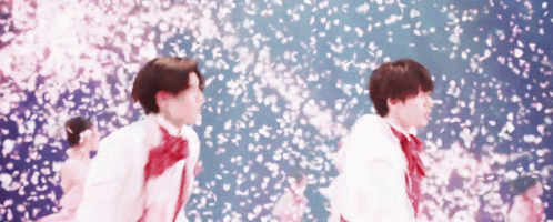 A Couple Of Young Men Are Standing In Front Of A Wall Of Cherry Blossoms . GIF