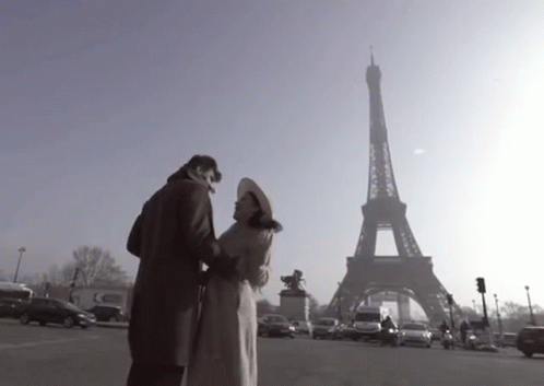 A Couple Standing In Front Of The Eiffel Tower In Paris GIF