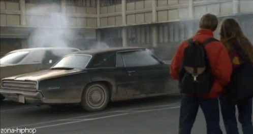 A Couple Standing Next To A Car That Has Smoke Coming Out Of It And The Words Zona-Hiphop On The Bottom GIF