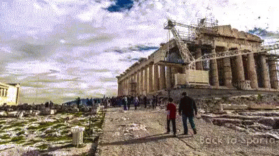 A Couple Walking In Front Of A Building With The Words Back To Sparta Written On The Bottom GIF