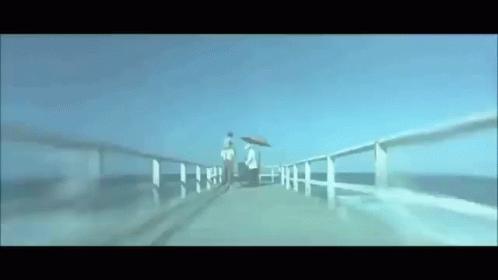 A Couple Walking On A Pier With Umbrellas GIF