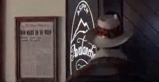 A Cowboy Hat Is Sitting On A Table Next To A Framed Newspaper And A Sign . GIF