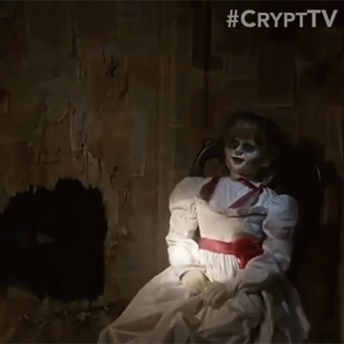 A Creepy Doll In A White Dress Is Sitting In A Chair GIF
