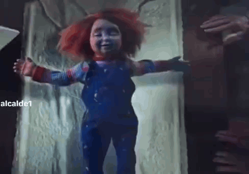 A Creepy Doll With Red Hair And Blue Overalls Is Standing In A Doorway With Its Arms Outstretched . GIF