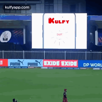 A Cricket Game Is Being Played In Front Of A Large Screen That Says Kulfy Out GIF