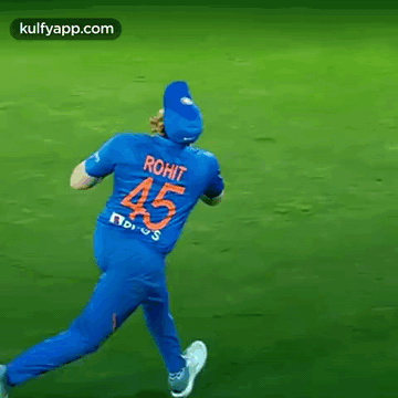 a cricket player wearing a blue jersey with the number 45 on the back is running on a field .