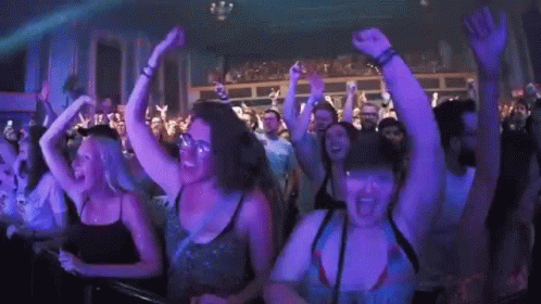 A Crowd Of People Are Dancing In A Club With Their Hands In The Air . GIF