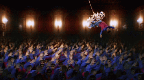 A Crowd Of People Are Dancing In A Dark Room With A Chandelier In The Background GIF