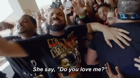 A Crowd Of People Are Gathered Around A Man Wearing A T-Shirt That Says " Do You Love Me " GIF