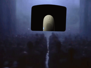 a crowd of people are gathered in a dark room with a microphone hanging from the ceiling