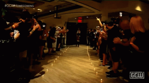 a crowd of people are gathered in a dark room with a sign that says gcw homecoming