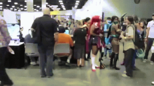 A Crowd Of People Are Gathered In A Room With A Man In An Orange Shirt Sitting At A Table GIF