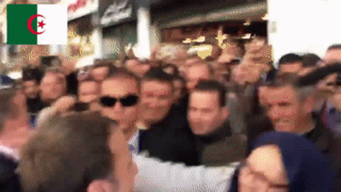 A Crowd Of People Are Gathered In Front Of A Flag That Says Algeria On It GIF