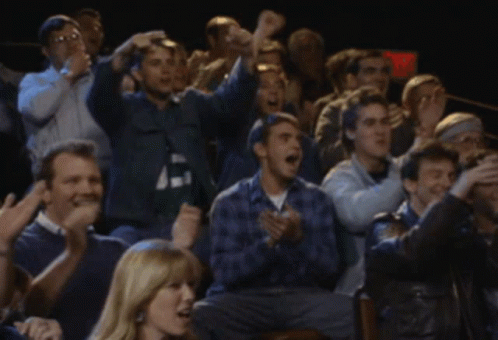 A Crowd Of People Are Sitting In A Dark Room With A Red Exit Sign In The Background GIF