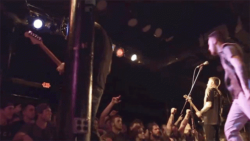A Crowd Of People Are Watching A Band Perform On Stage With An Exit Sign In The Background GIF