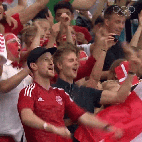 A Crowd Of People Cheering In A Stadium With The Olympic Rings In The Background . GIF