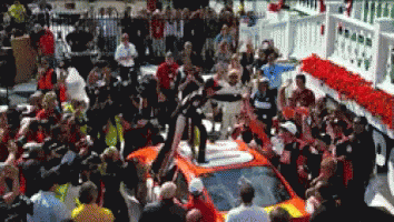 A Crowd Of People Gathered Around A Race Car GIF