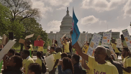 A Crowd Of People Holding Signs Including One That Says Save The Kids GIF