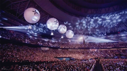 A Crowd Of People In A Stadium With Balloons Hanging From The Ceiling That Have A Cross On Them GIF