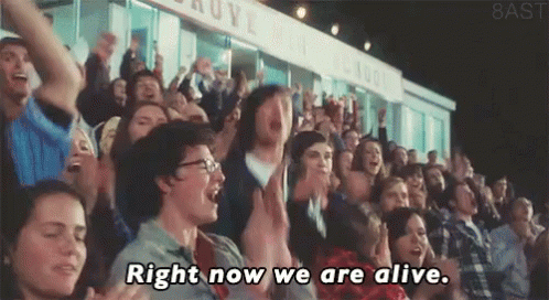 A Crowd Of People In A Stadium With The Words Right Now We Are Alive Written On The Screen GIF