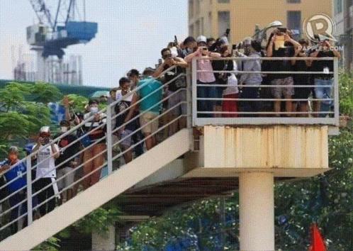 A Crowd Of People Standing On A Bridge With A R On The Bottom Left GIF