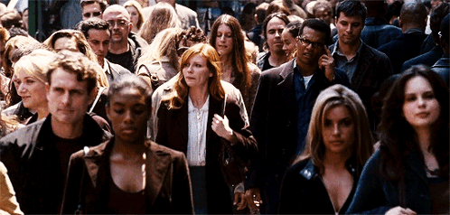 A Crowd Of People Walking Down A Street Including A Woman With Red Hair GIF