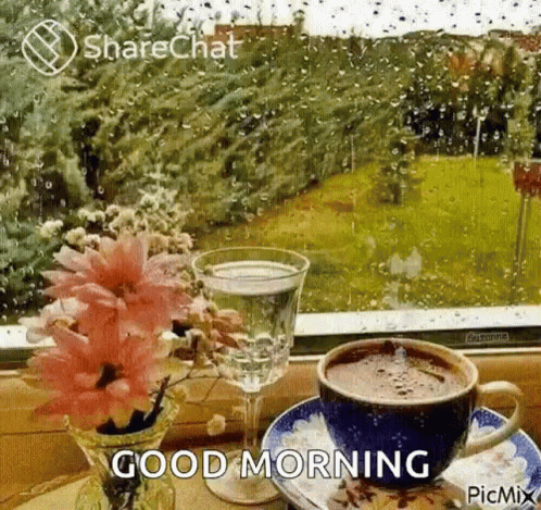 A Cup Of Coffee And A Glass Of Water Are On A Table In Front Of A Window With Rain Drops . GIF