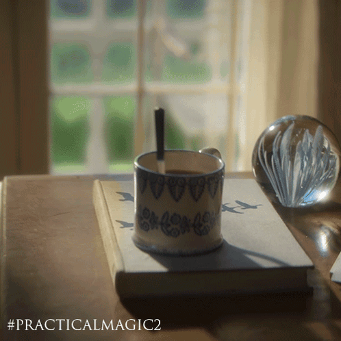 a cup of coffee sits on top of a book called practical magic
