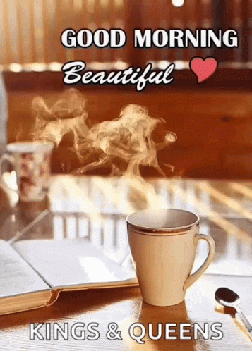 A Cup Of Coffee With Steam Coming Out Of It Is On A Table With A Book And A Spoon . GIF