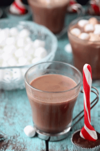 A Cup Of Hot Chocolate Next To A Candy Cane On A Table GIF