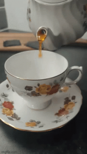 A Cup Of Tea Is Being Poured Into A Saucer With Flowers On It GIF