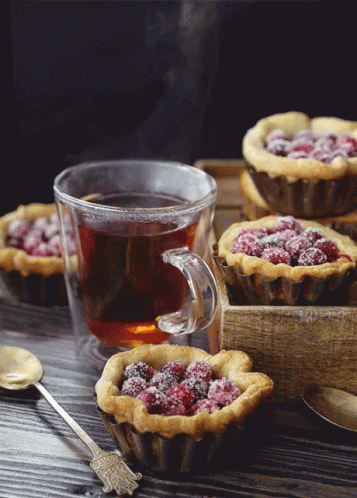 a cup of tea sits on a table next to a tray of muffins