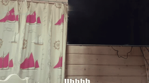 a curtain with sailboats and steering wheels hangs next to a flat screen tv