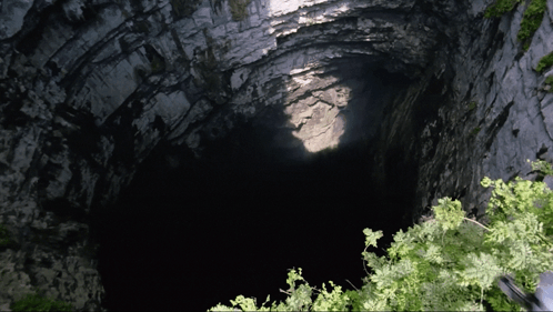 A Dark Cave With A Light Coming Out Of The Ceiling GIF