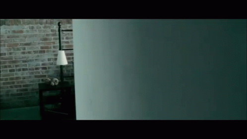 A Dark Room With A Brick Wall And A Lamp On A Table GIF
