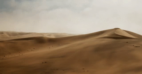 A Desert Landscape With Sand Dunes And Mountains In The Distance GIF