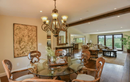 A Dining Room With A Round Glass Table And Chairs And A Chandelier GIF