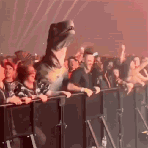 A Dinosaur Is Standing In Front Of A Crowd At A Concert . GIF