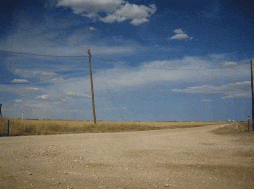 A Dirt Road Going Through A Field With Telephone Poles GIF