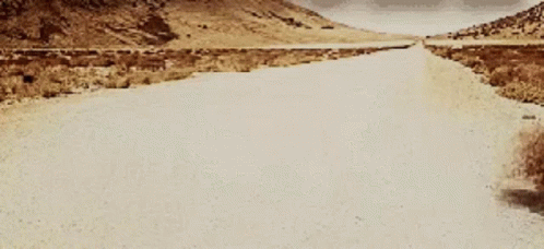 A Dirt Road With Mountains In The Background GIF