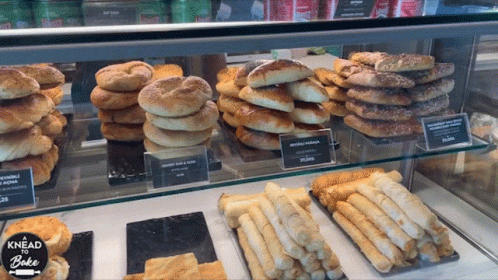 A Display Case Filled With A Variety Of Breads And Pastries With The Words Knead To Bake On The Bottom GIF