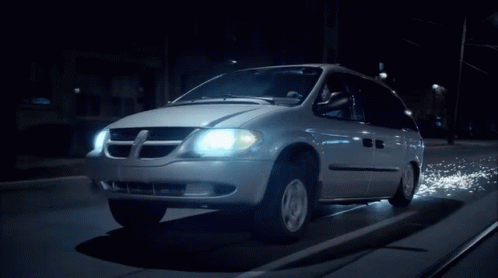 A Dodge Minivan Is Driving Down A Dark Street At Night GIF