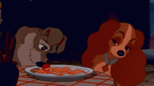 a dog and a woman are sitting at a table eating spaghetti .