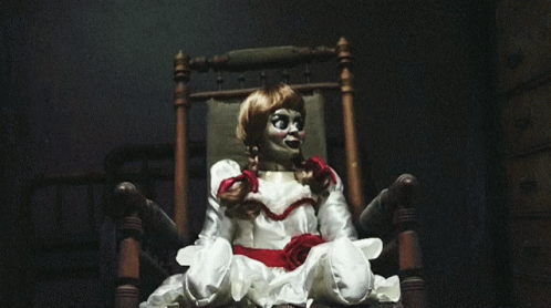 A Doll Is Sitting In A Chair With A Red Bow Around Her Neck GIF