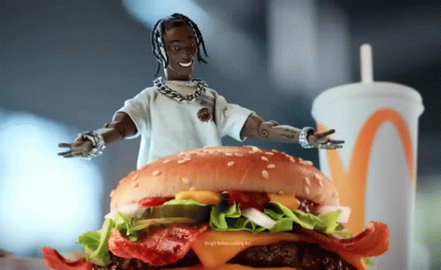 A Doll Is Standing On Top Of A Hamburger With A Drink In The Background GIF