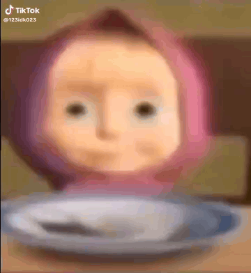 A Doll With A Pink Hat Is Sitting On A Plate With A Spoon . GIF