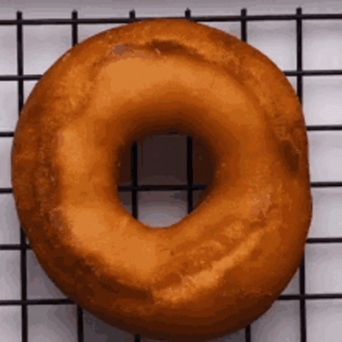 A Donut Is Sitting On A Wire Rack On A Table . GIF