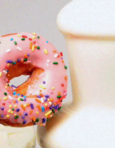 A Donut With Pink Frosting And Sprinkles Next To A Vase GIF